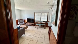 A living room with a TV, sofa, and dining area with chairs and a table. - One Particular Cottage - Next to Margaritaville (Fort Myers Beach)