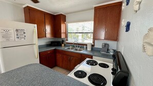 A compact kitchen with wooden cabinets, a white refrigerator, a stove, and a sink. - One Particular Cottage - Next to Margaritaville (Fort Myers Beach)