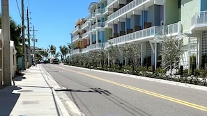 A multi-story hotel with balconies, a sidewalk, and palm trees.