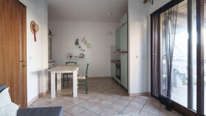 A small kitchen with a dining table and chairs, a refrigerator, and a window with curtains.