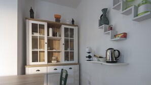 A kitchen with a wooden cabinet, a kettle, and a shelf with kitchen items.