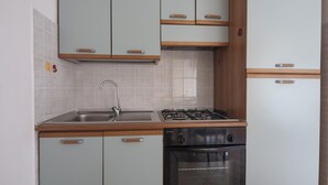 A compact kitchen with a sink, stove, oven, and light green cabinets with wooden handles.