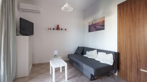 A small, clean room with a grey sofa, a white table, a TV, and a painting on the wall.