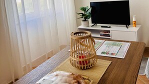 A room with a wooden table, a TV on a white stand, a plant, and a window with sheer curtains. - Casa Olbia Centro in Olbia (Olbia)