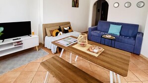 A living room with a TV, a sofa, a coffee table, and a bed. - Casa Olbia Centro in Olbia (Olbia)