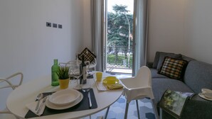 Un espace de vie compact comprenant un coin repas, un canapé et un balcon avec vue sur les arbres.
