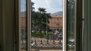 Une vue depuis un balcon doté d’une rambarde en métal, donnant sur une rue où sont garées des voitures et sur un immeuble avec de nombreuses fenêtres.