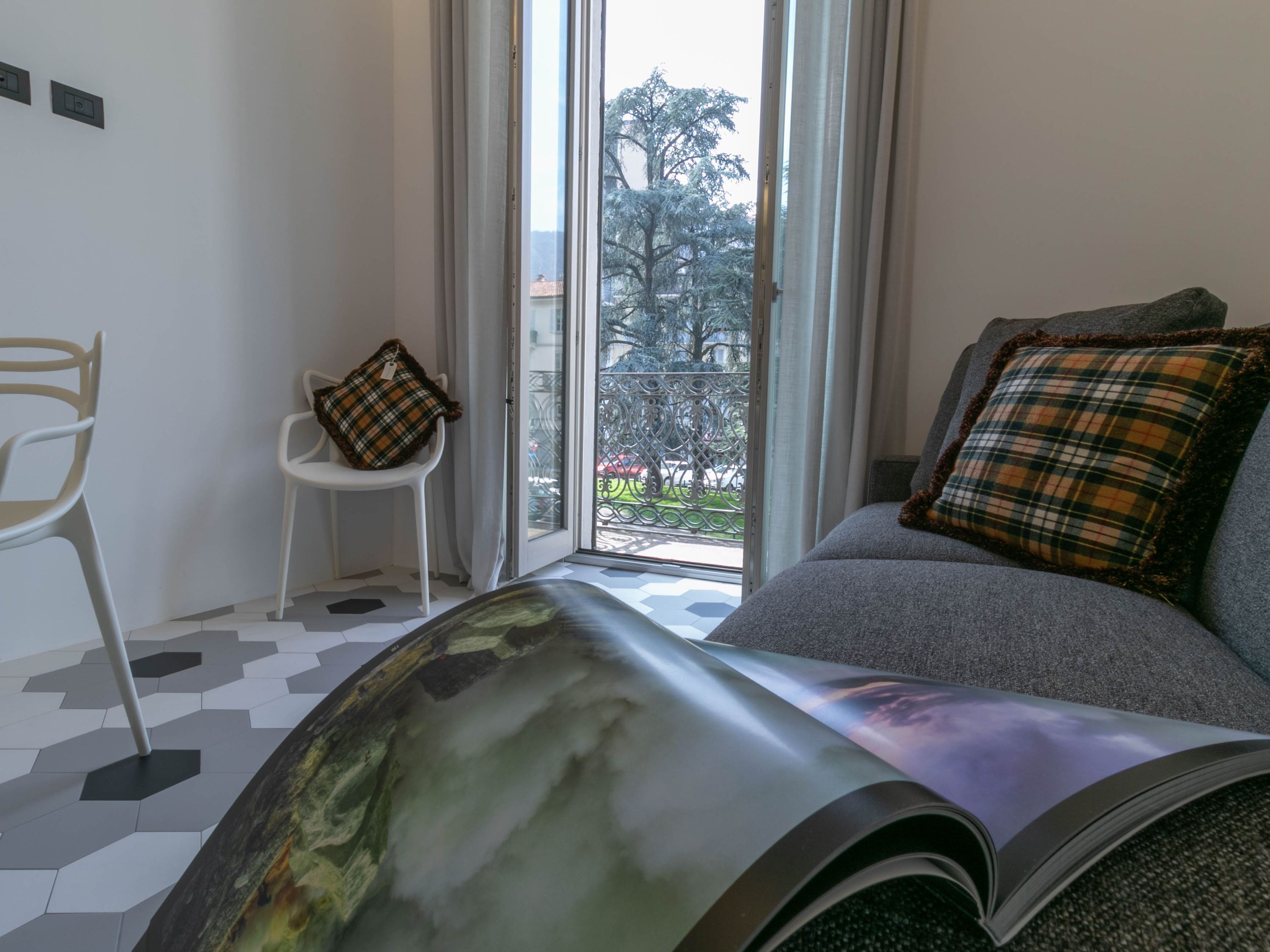 Een moderne kamer met een grijze bank, een witte stoel en uitzicht door een glazen deur op een balkon.
