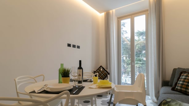 Un coin repas moderne avec une table ronde, des chaises, une plante en pot, des verres à vin et une bouteille.