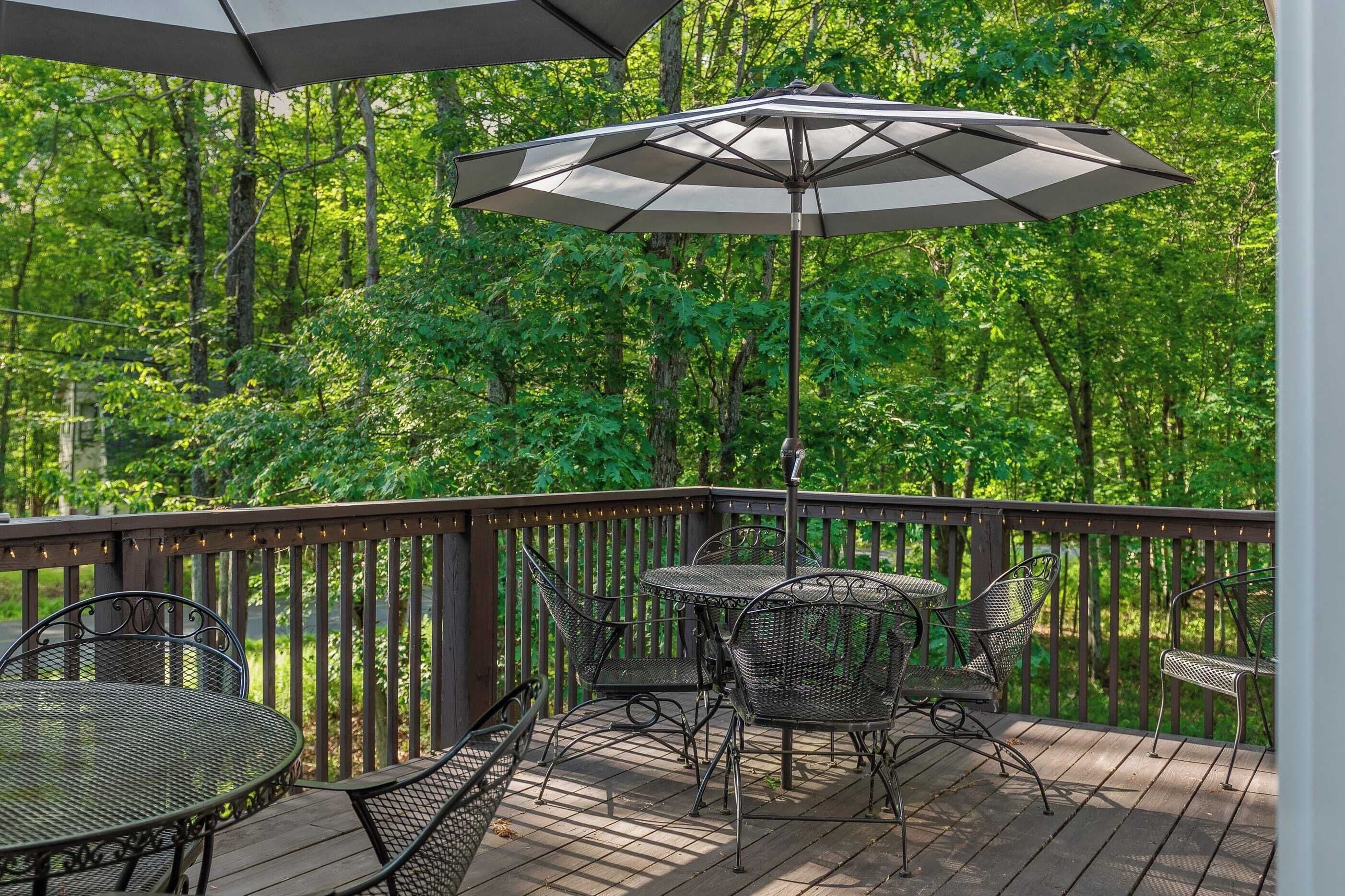 A wooden deck with metal chairs and a table, surrounded by a wooden railing and a large umbrella.