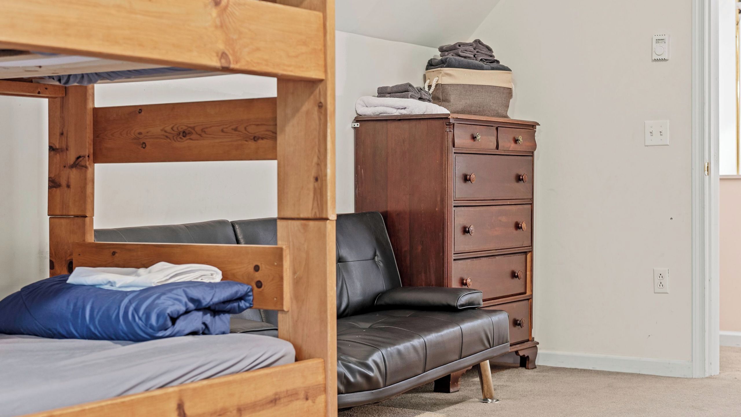 A bunk bed with a wooden headboard, a black leather sofa, and a wooden dresser with drawers.