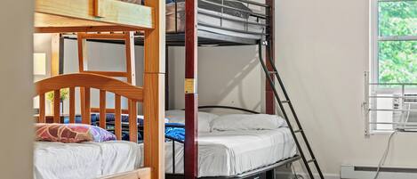 Habitación con literas, ventana, radiador y una silla de madera.