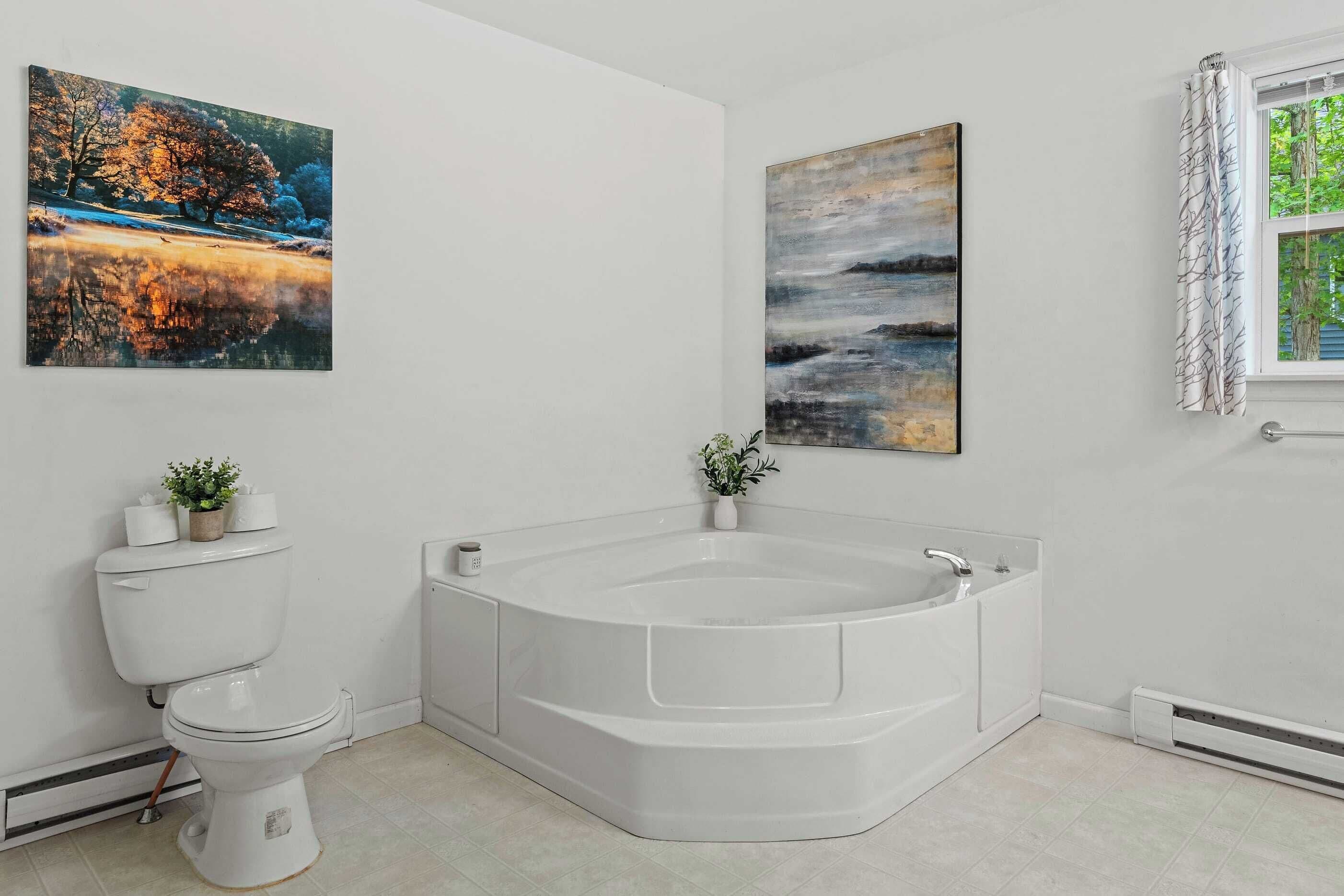 A bathroom with a toilet, a freestanding bathtub, and two wall-mounted paintings.