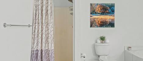 A bathroom with a shower curtain, toilet, and a painting on the wall.