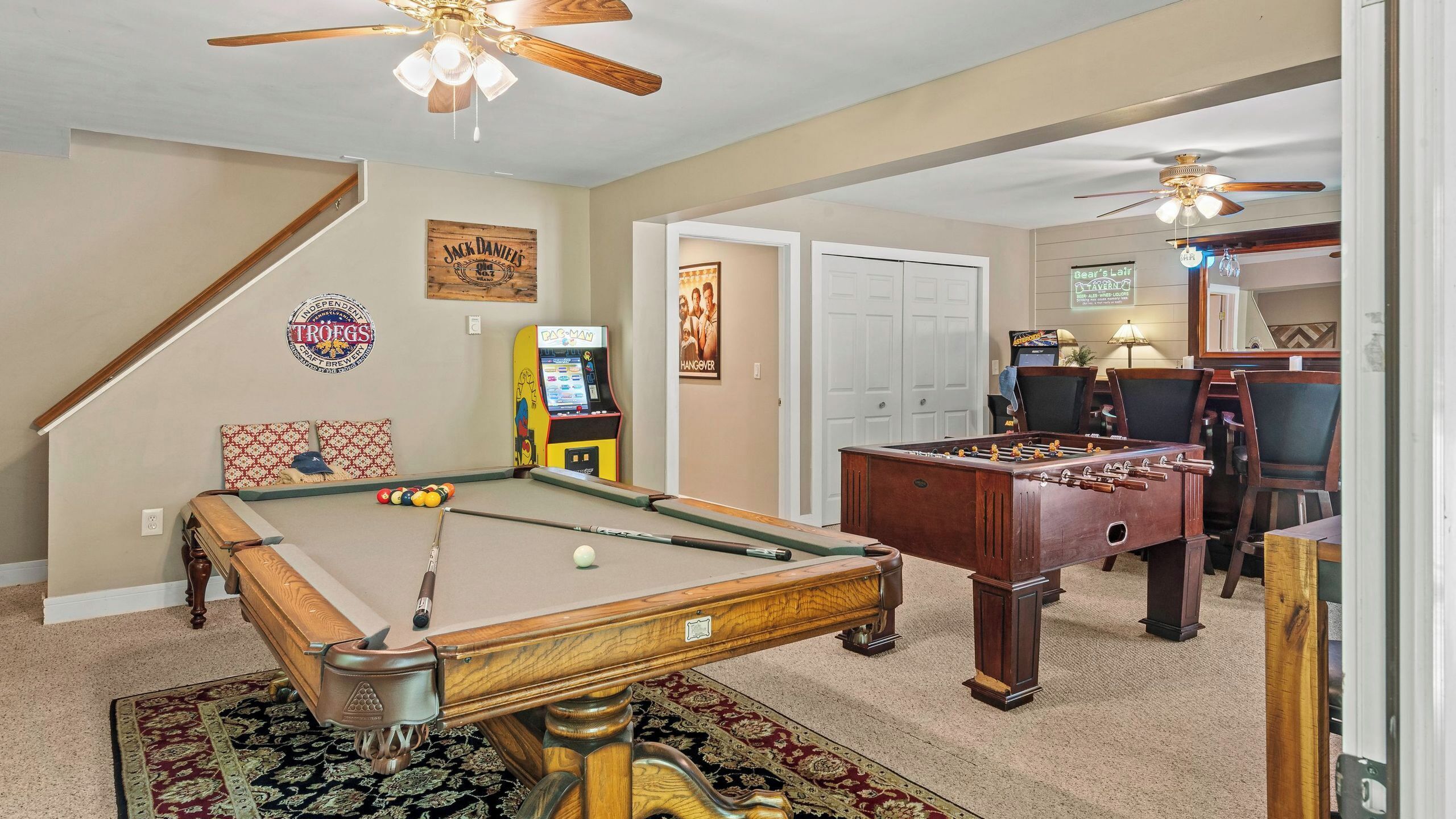 A pool table, foosball table, and arcade games in a room with a staircase and a door leading to another area.