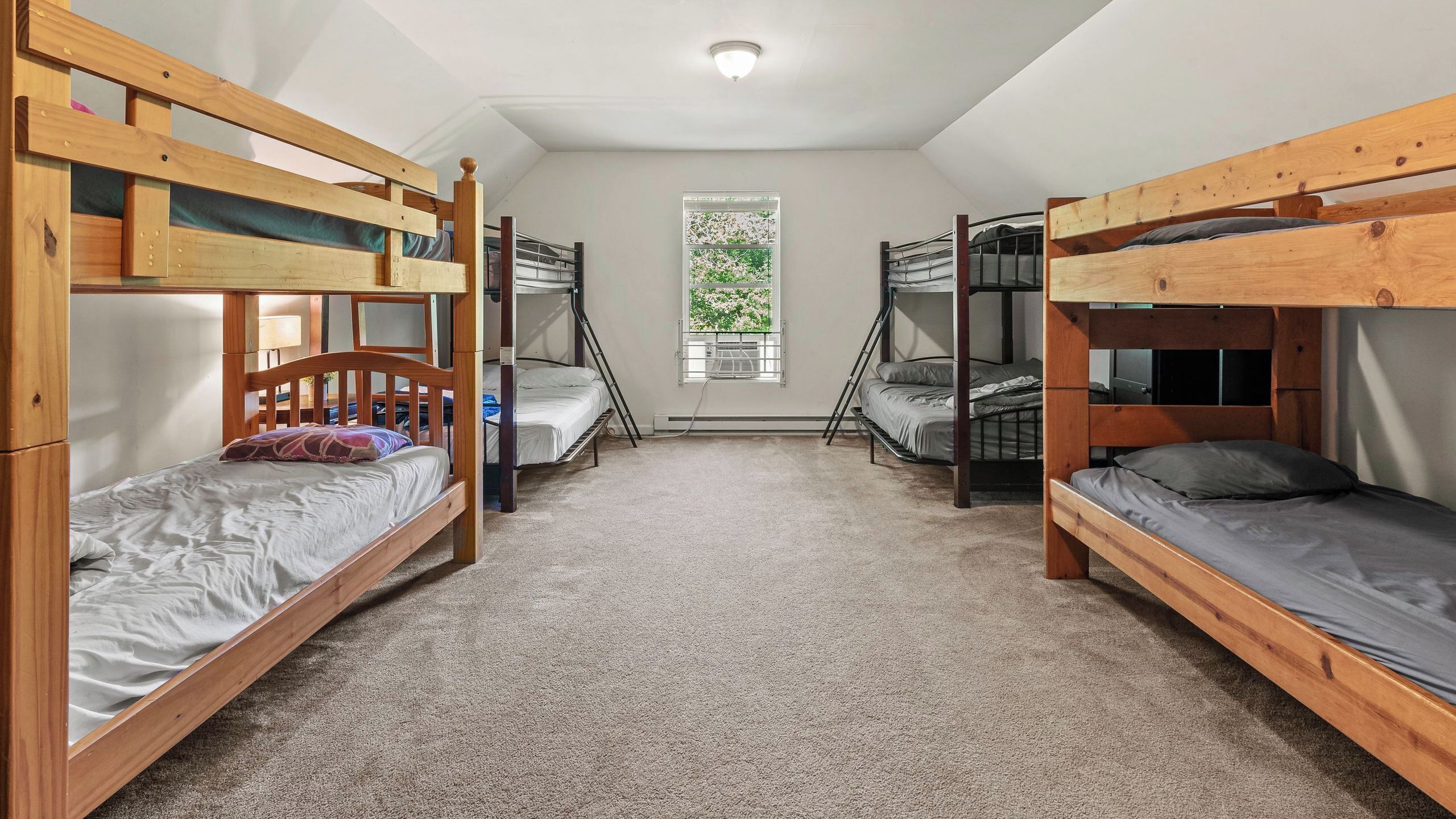 A dormitory room with bunk beds, carpeted floor, and a window with a view of greenery.