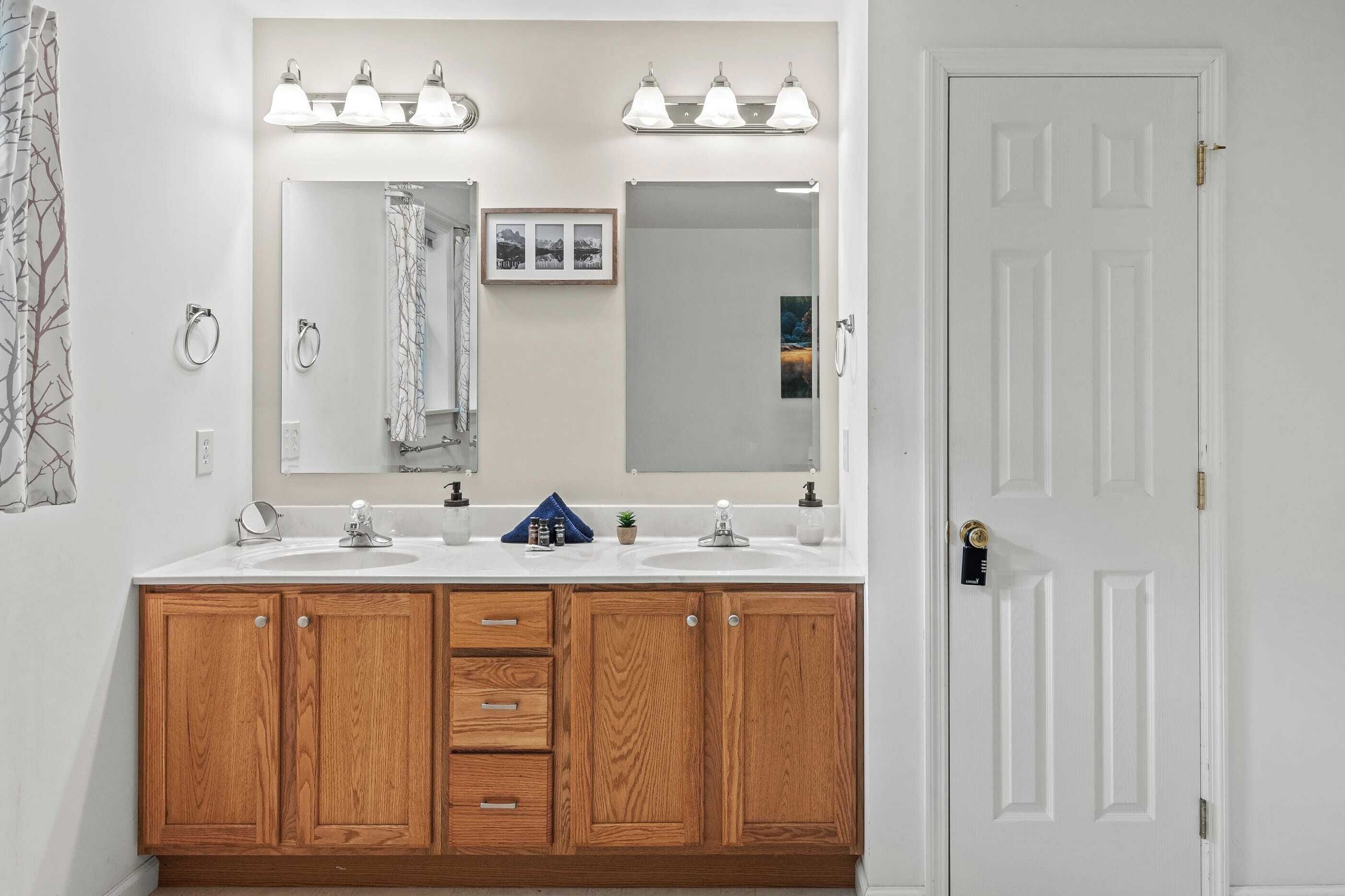 A bathroom with two sinks, wooden cabinets, a large mirror, and a door.