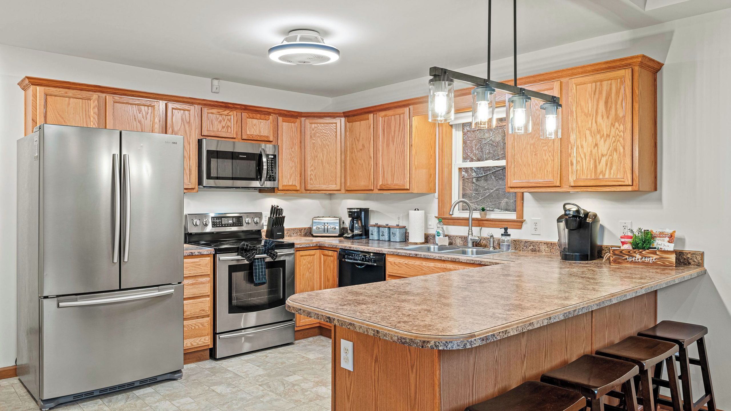 A modern kitchen with wooden cabinets, stainless steel appliances, granite countertops, and a bar area.