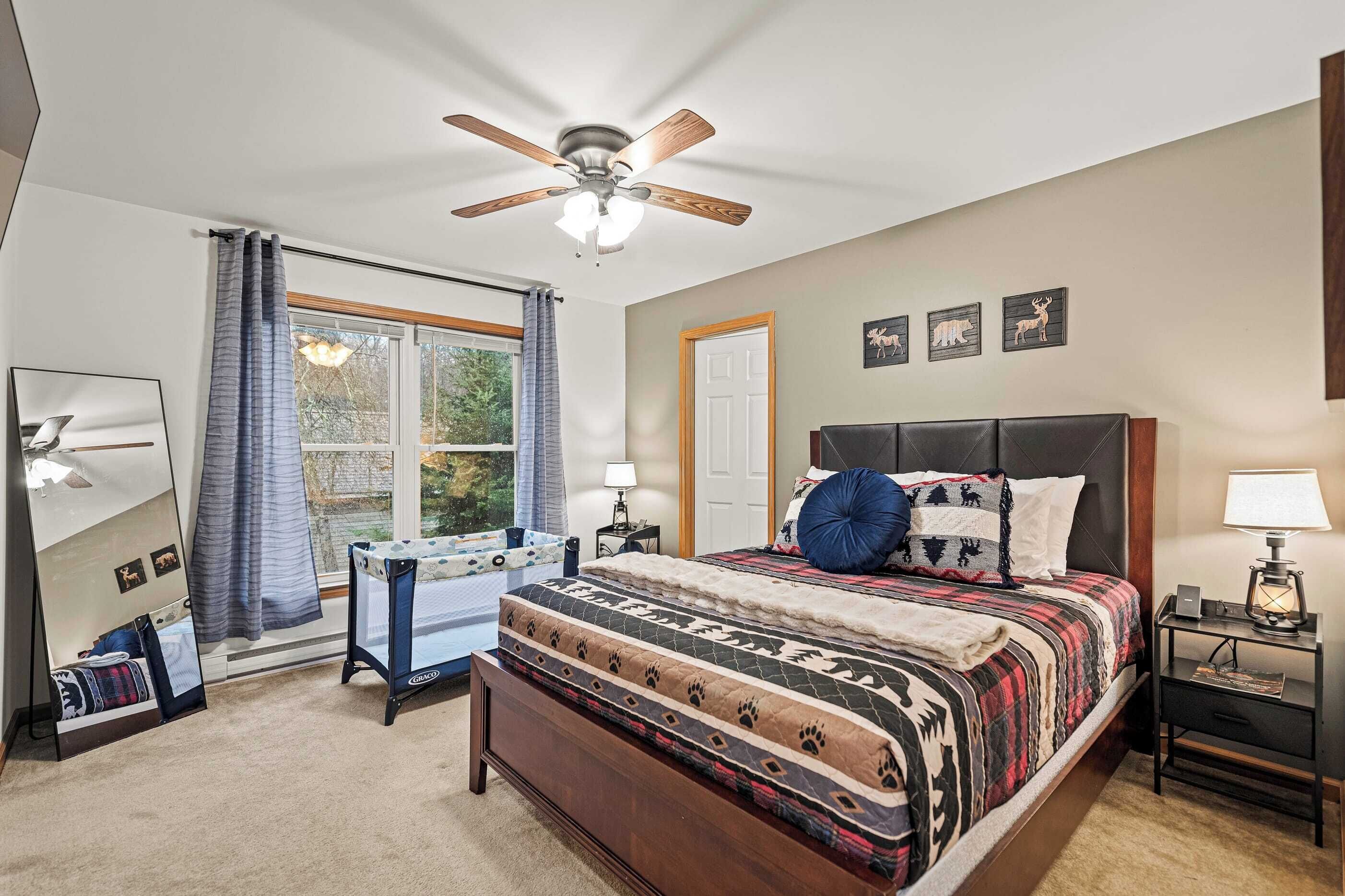 A bedroom with a bed, a ceiling fan, a nightstand, a desk, and a window with curtains.