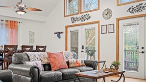 A living room with a leather sofa, a coffee table, and a dining area with chairs and a table. There are decorative wall art pieces and a ceiling fan. - Mews Mountain House by Avantstay Walk to Beach, Hot Tub, Game Room (Albrightsville)