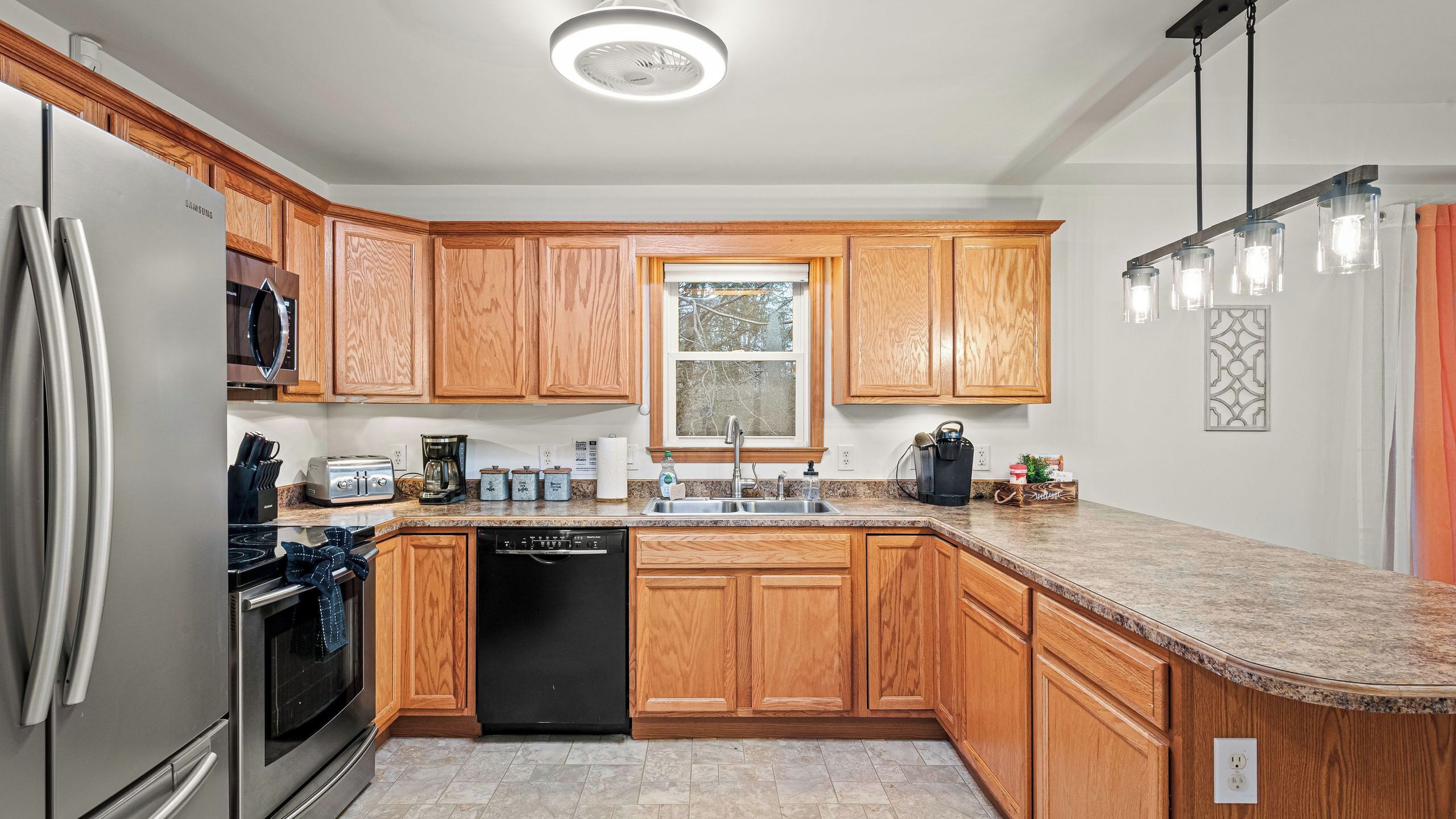 A modern kitchen with wooden cabinets, stainless steel appliances, a granite countertop, and a window with a view.
