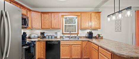 A modern kitchen with wooden cabinets, stainless steel appliances, a granite countertop, and a window with a view.