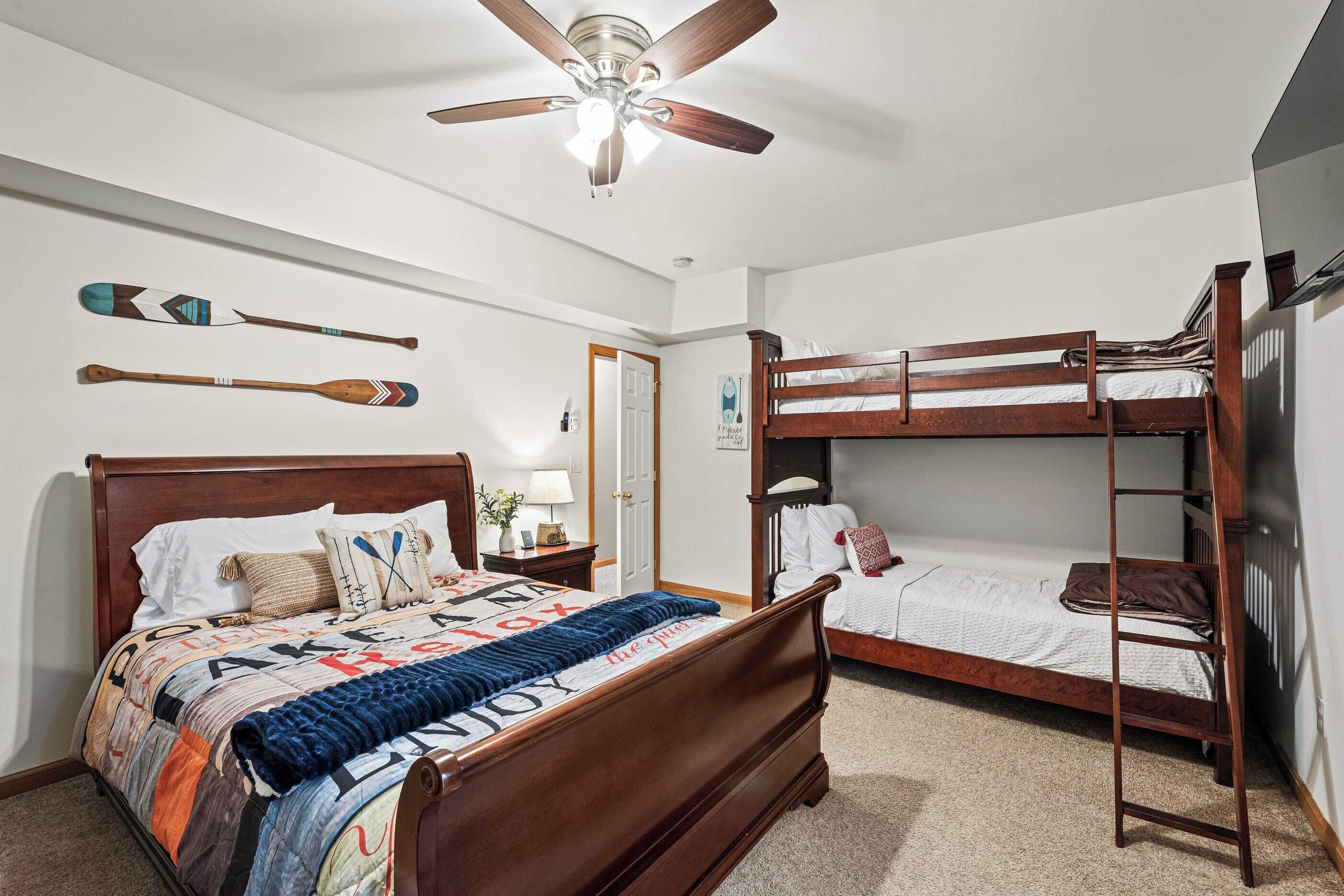 A bedroom with a wooden bed, a bunk bed, a ceiling fan, and wall-mounted paddles.