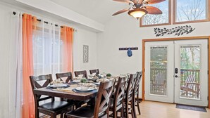 A dining area with a table set for six, wooden chairs, a ceiling fan, and a view through a glass door to the outside. - Mews Mountain House by Avantstay Walk to Beach, Hot Tub, Game Room (Albrightsville)