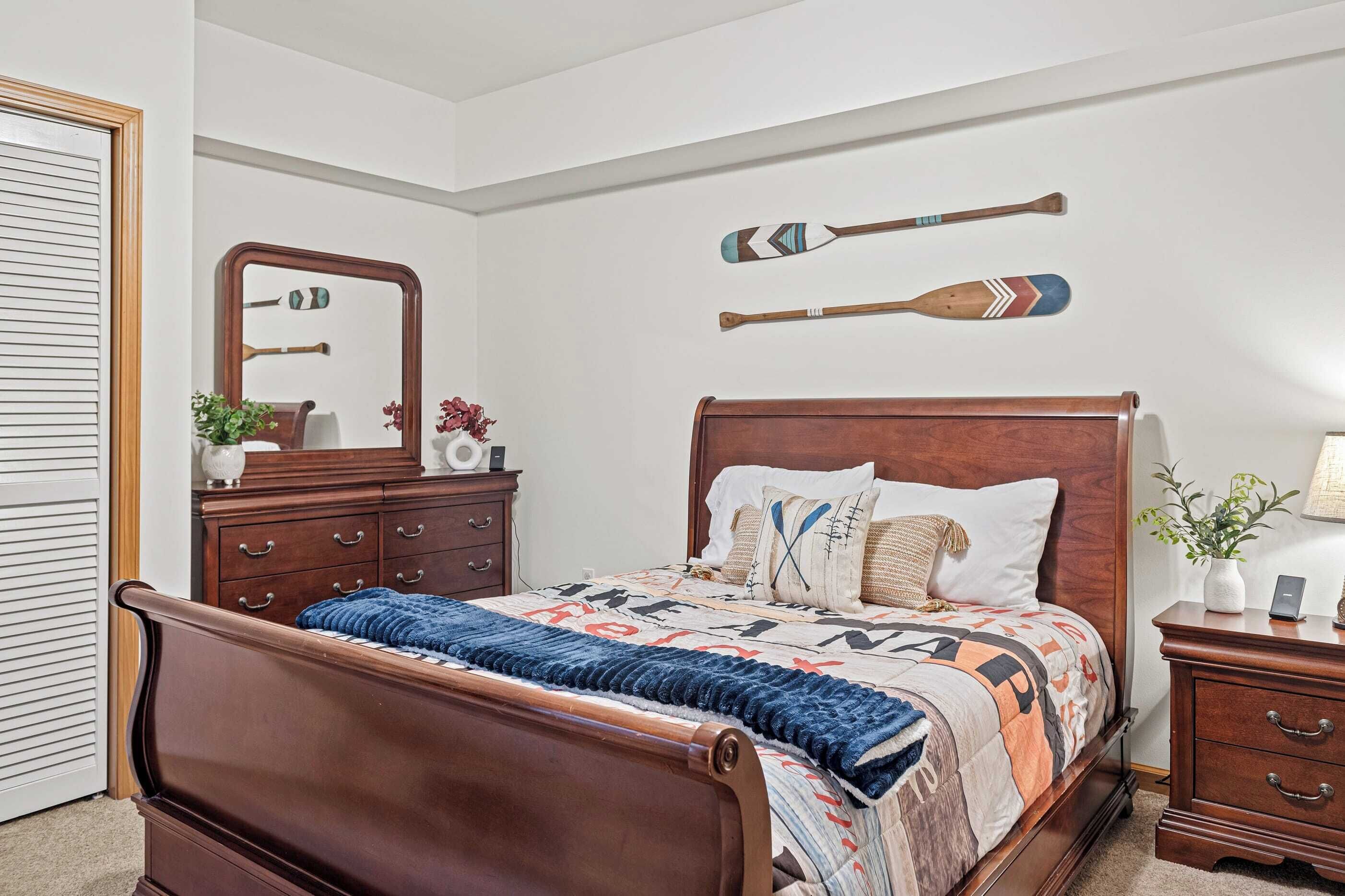 A bedroom with a wooden bed, a dresser, a mirror, and two wall-mounted paddles.