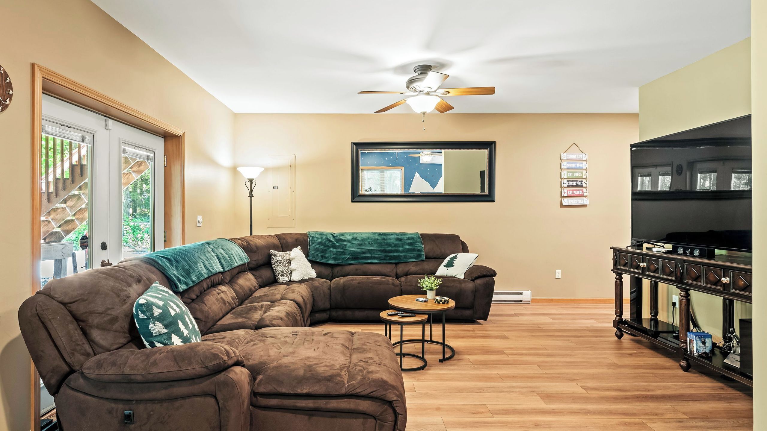 Un salon comprenant un canapé d’angle, un ventilateur de plafond, un téléviseur à écran plat et un meuble en bois.