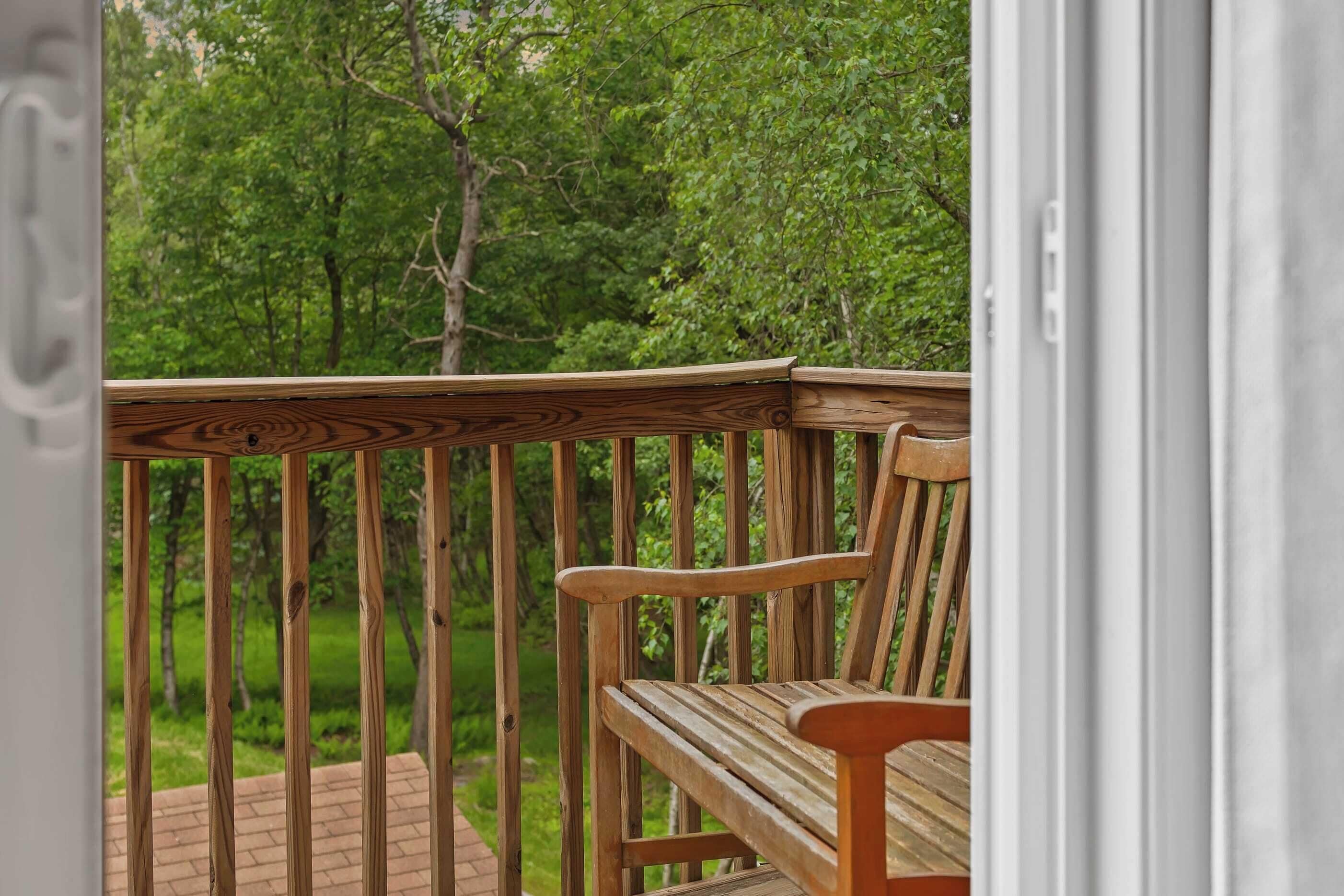 A wooden deck with a bench, surrounded by lush greenery.