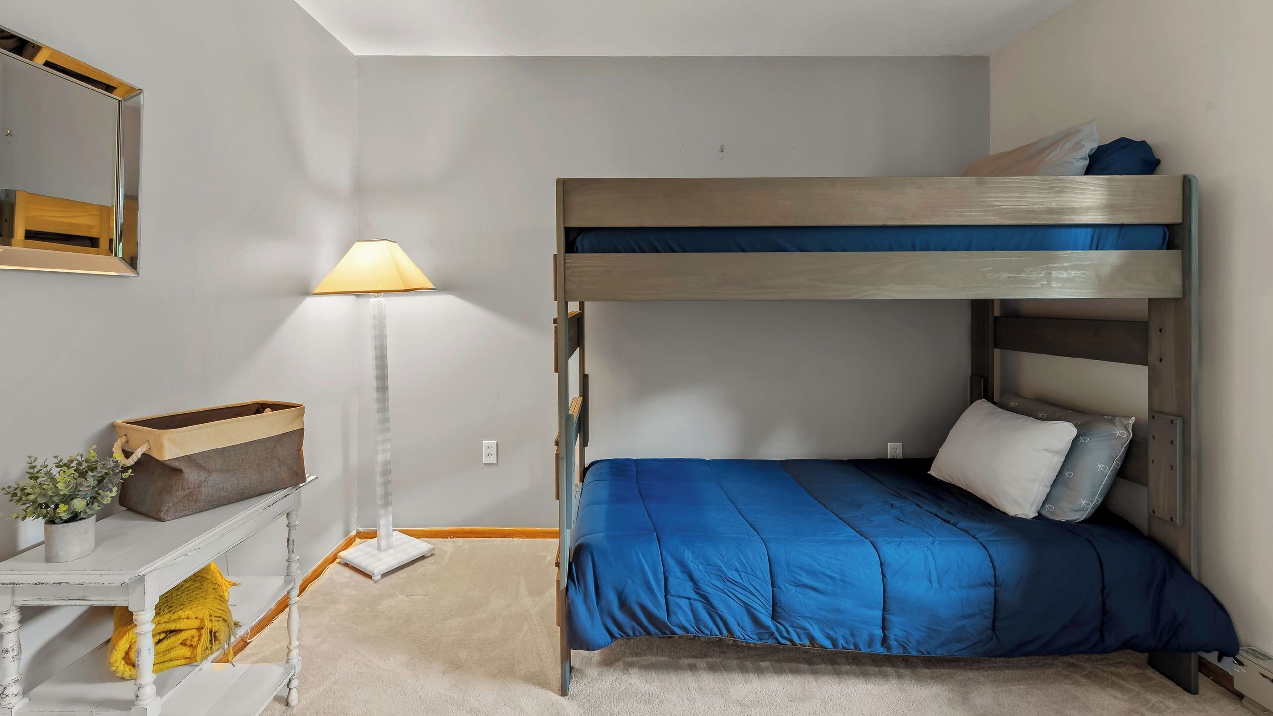 Ein Stockbett mit blauer Matratze, ein Nachttisch mit Lampe und ein kleiner Topf mit Pflanze.