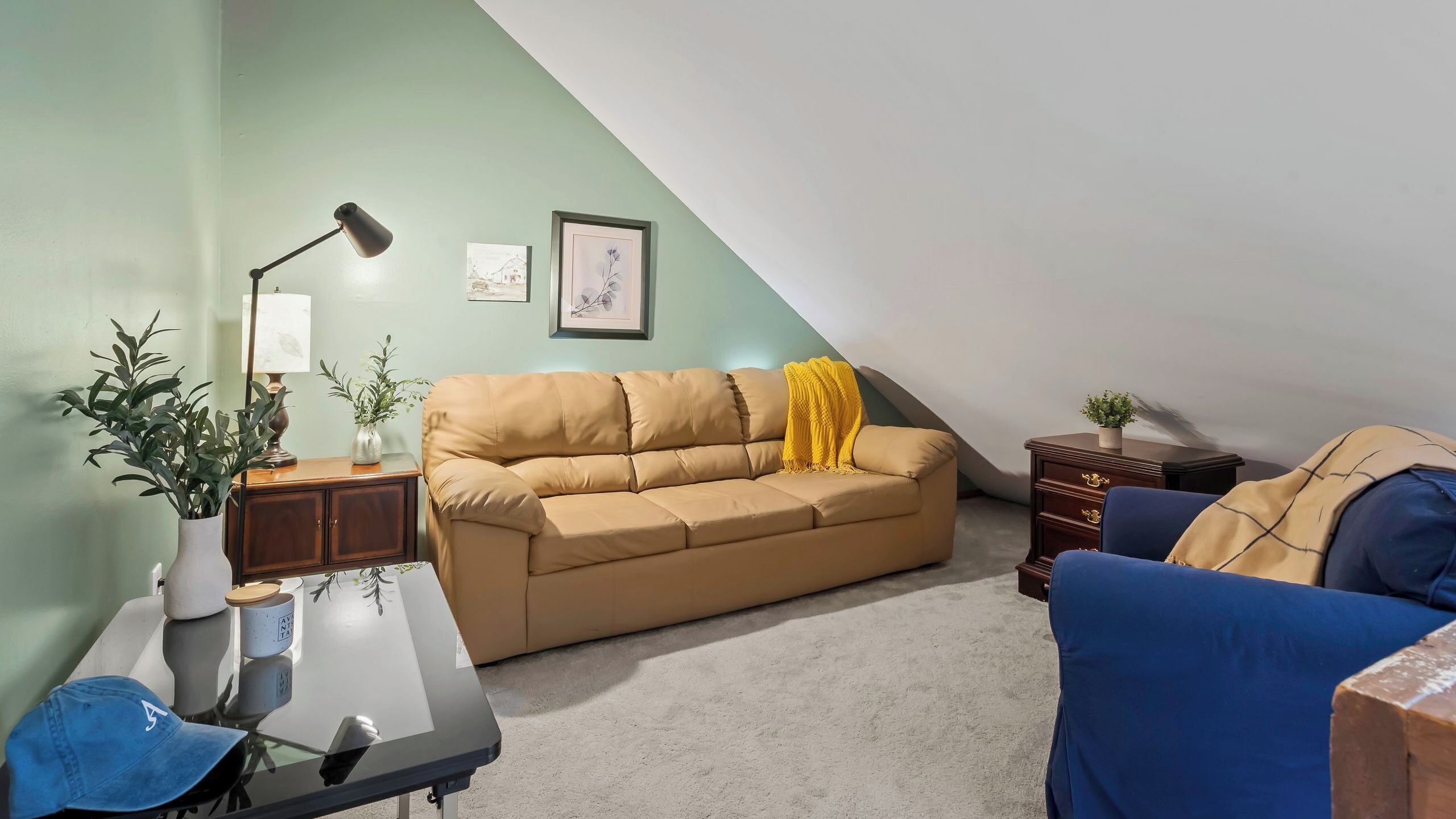 A cozy living room with a sofa, a small table with a lamp, a blue chair, and a plant.