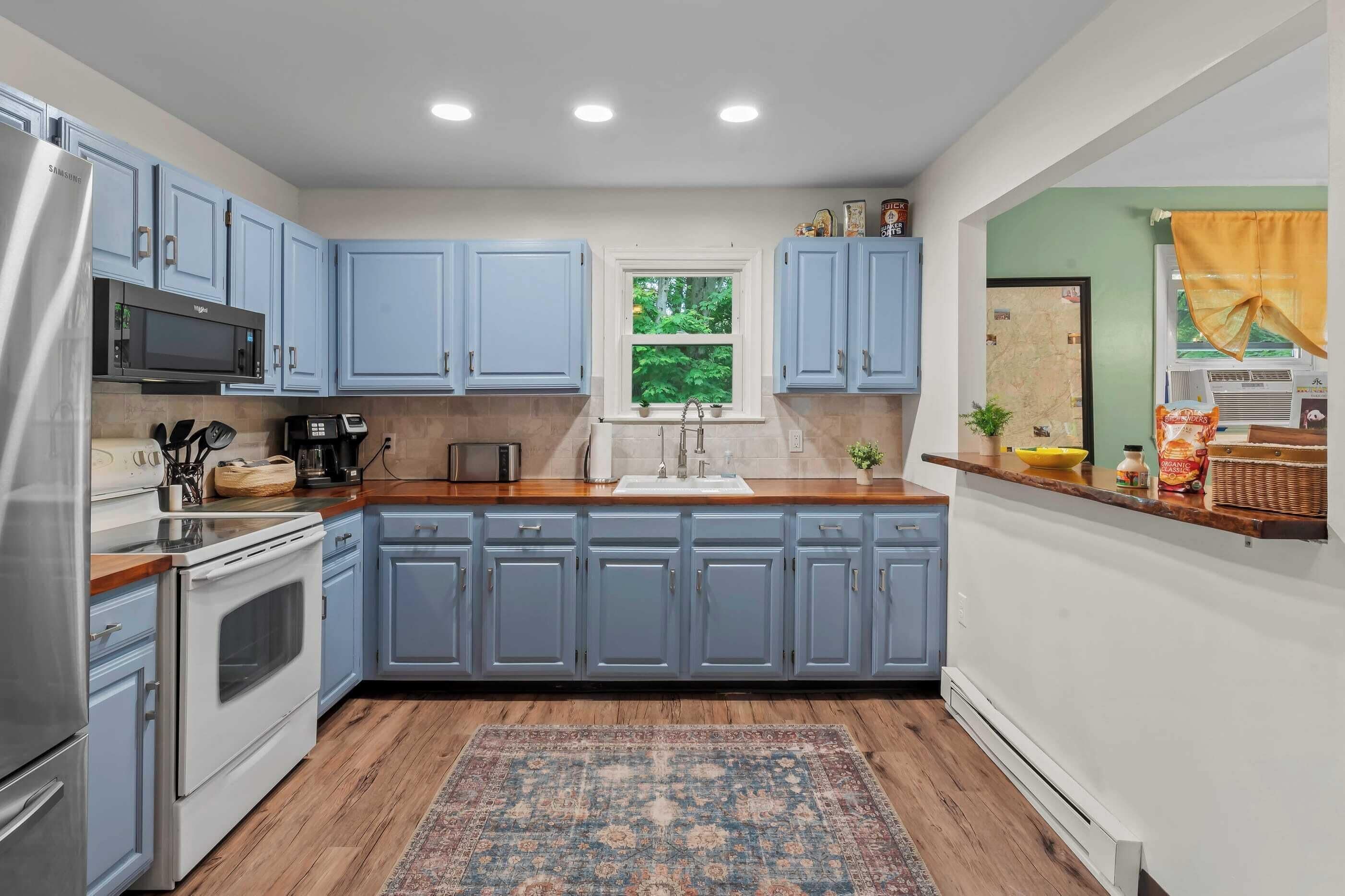 A modern kitchen with blue cabinets, stainless steel appliances, a wooden countertop, and a patterned rug.