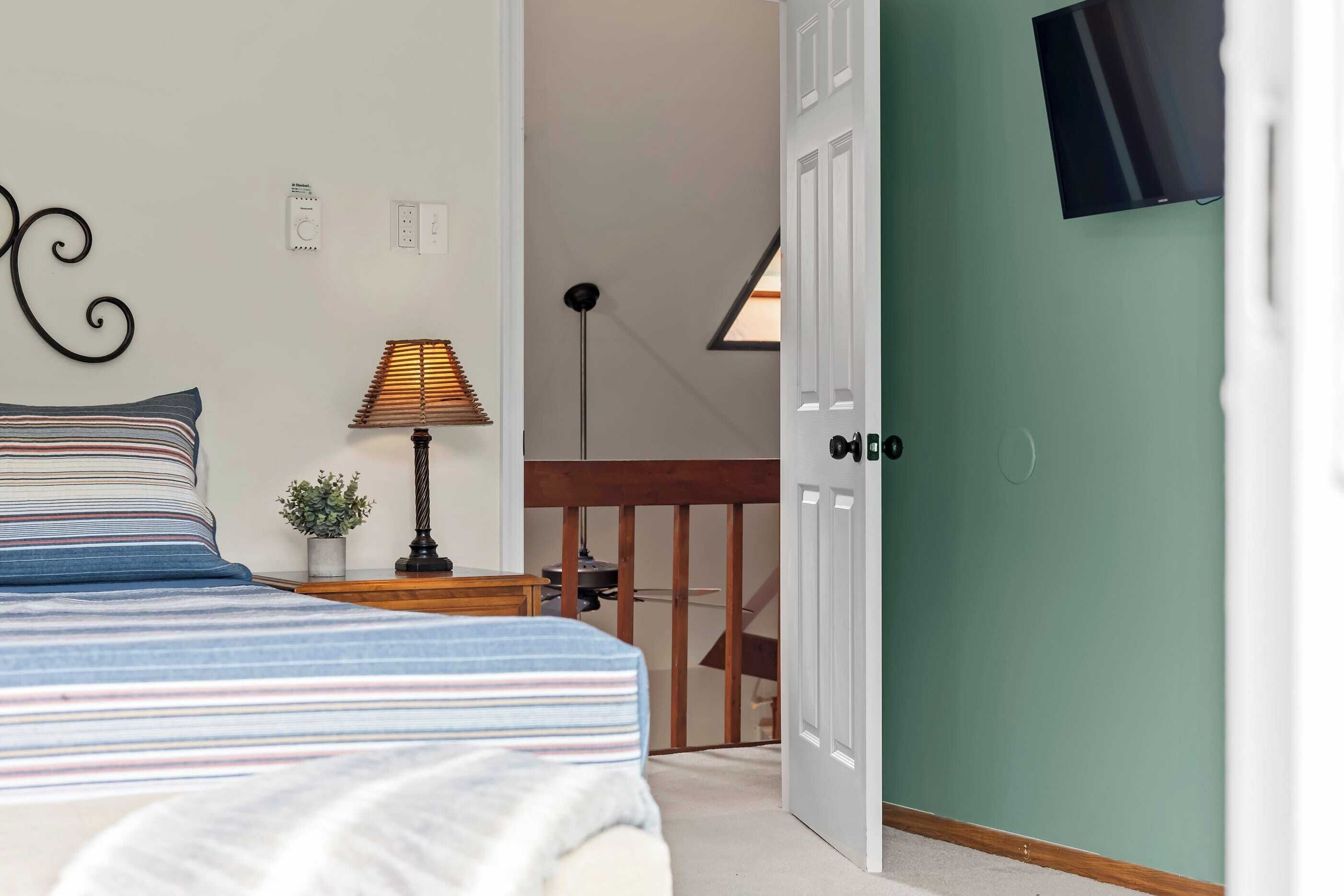 Ein Schlafzimmer mit einem Bett, einer Lampe, einer kleinen Pflanze und einem Fernseher an der Wand.