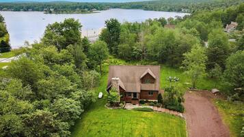 A cabin with a stone chimney, surrounded by a well-maintained lawn and a gravel driveway.
