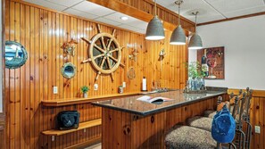 A wooden-paneled bar area with a ship's wheel, pendant lights, and bar stools. - Entertainer's Home w/ Deck, Game Room & Hot Tub Lake View Retreat by Avantstay (Albrightsville)