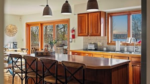 A spacious kitchen with wooden cabinets, a large island with bar stools, and a view of the outdoors through large windows.