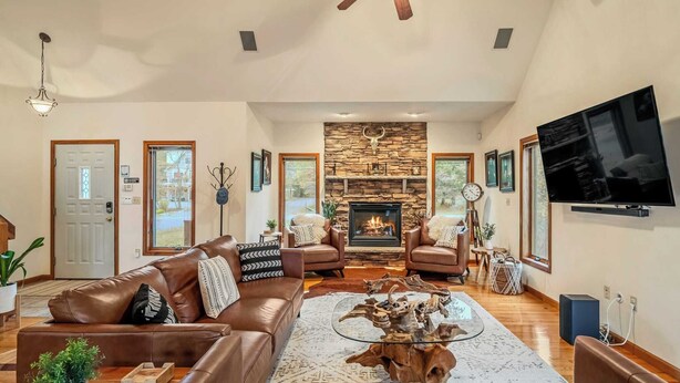A spacious living room with leather sofas, a glass coffee table, a stone fireplace, and a flat-screen TV.