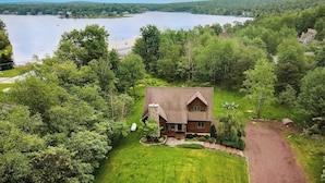 A cabin with a stone chimney, surrounded by a well-maintained lawn and a gravel driveway.