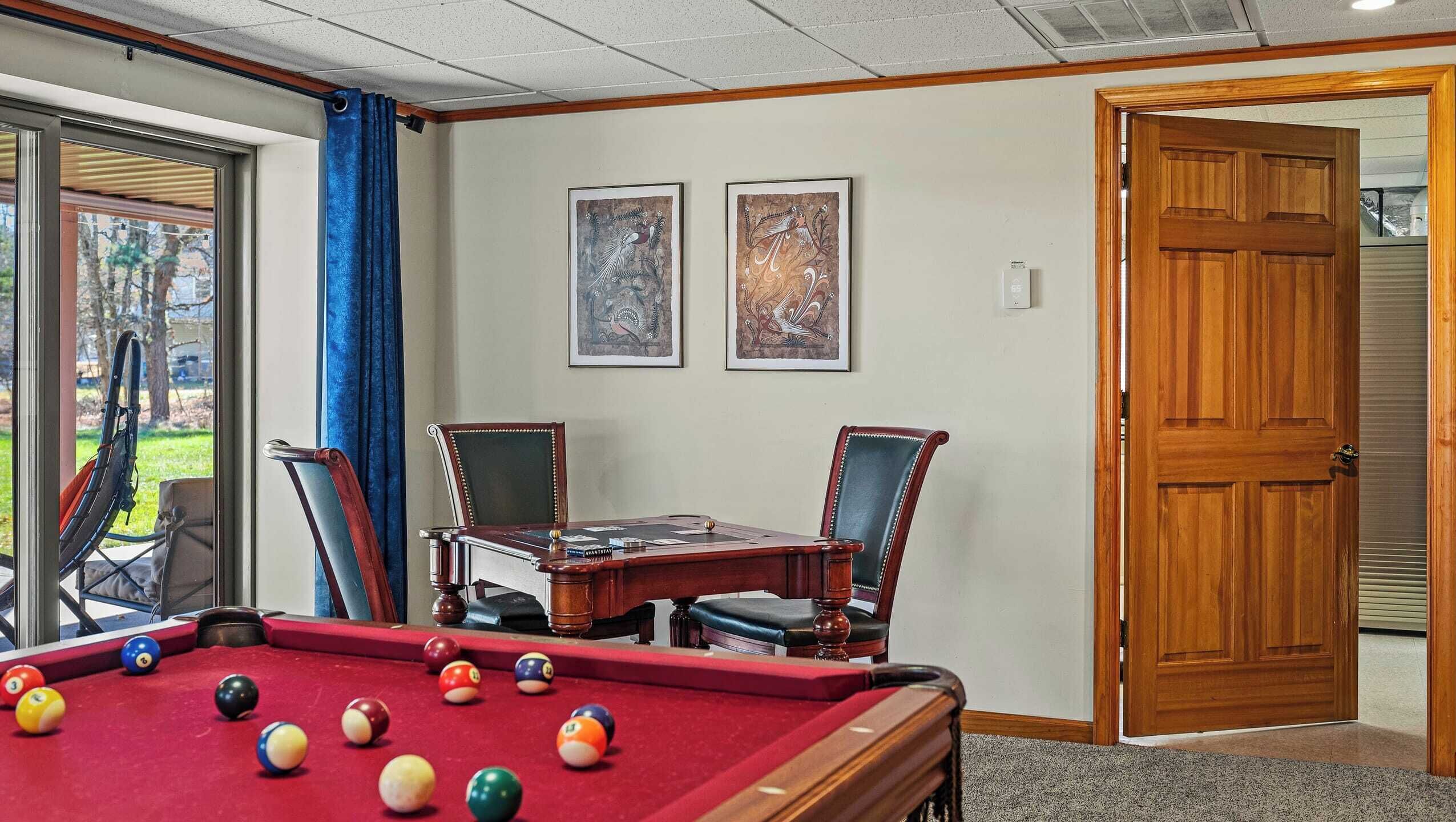 A pool table with balls, two framed artworks, and a wooden door.