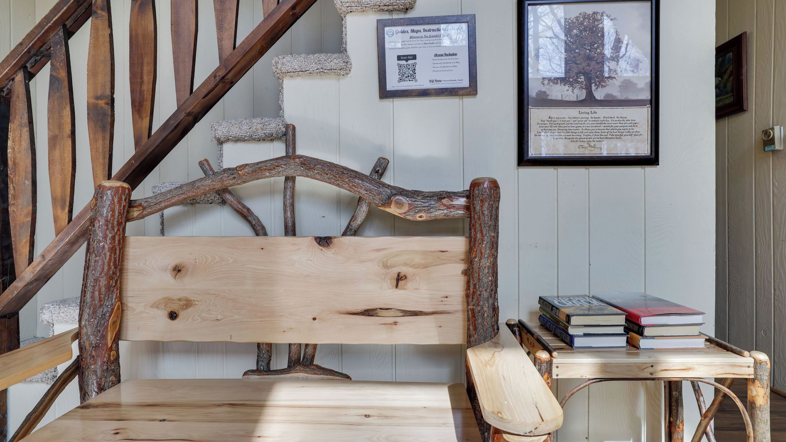 Un banc en bois rustique doté d’un dossier sculpté, une petite table avec des livres et un panneau d’information encadré accroché au mur.
