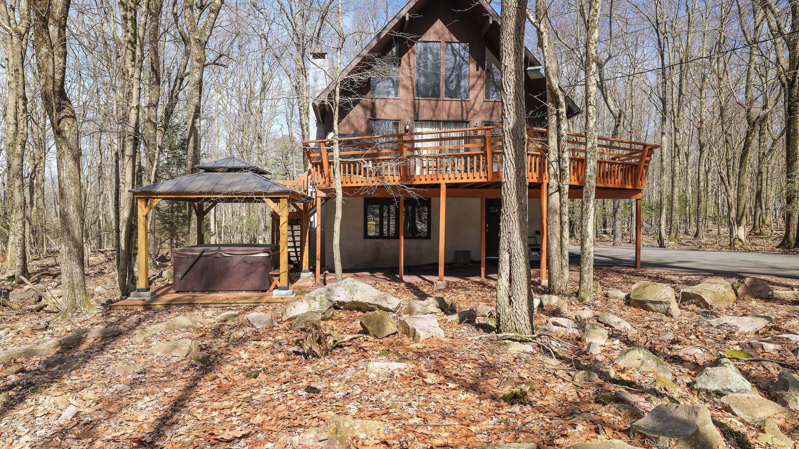 A cabin with a hot tub, wooden deck, and a covered seating area in a forest.