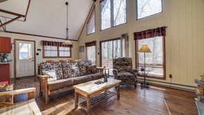 A spacious living area with a sofa, armchair, and wooden coffee table. Large windows provide natural light and views.