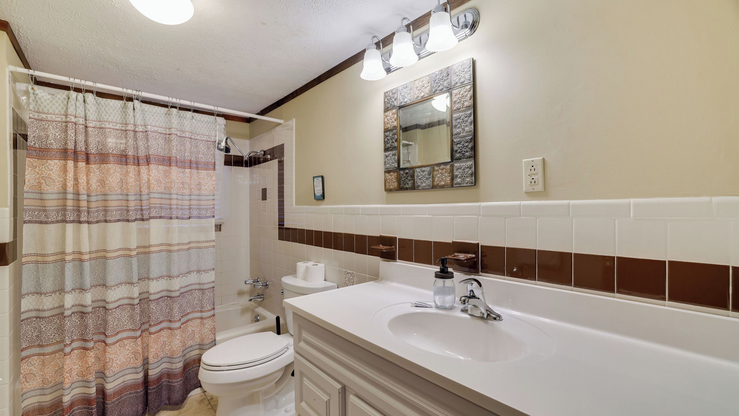 Une salle de bain équipée d’un rideau de douche, de toilettes, d’un lavabo et d’un miroir.