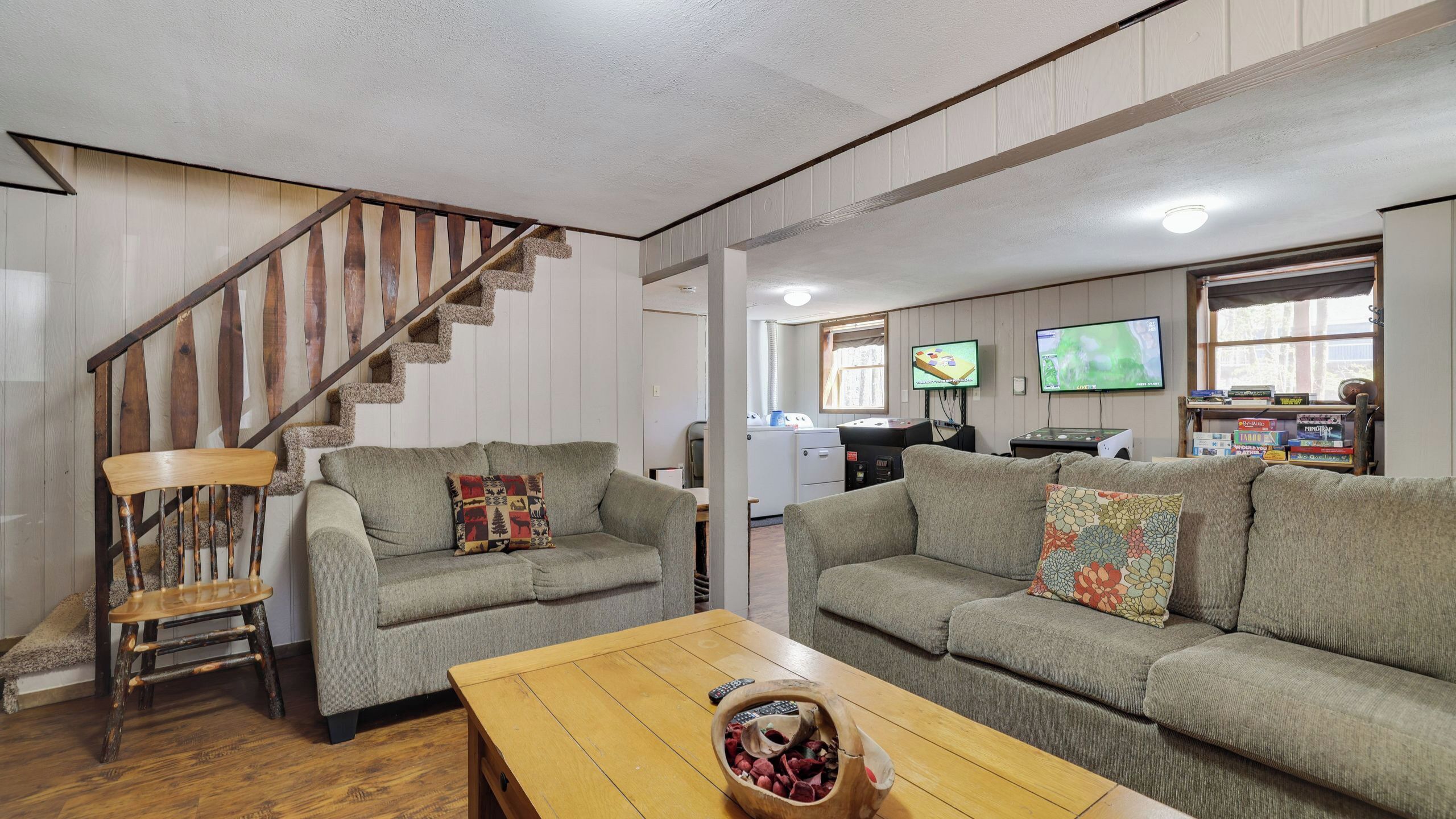 A living room with two sofas, a wooden coffee table, a wooden chair, and a staircase.