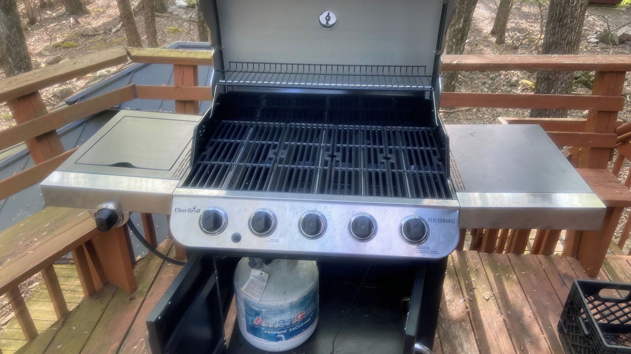 Uma churrasqueira a gás Char-Broil com quatro queimadores, um tanque de propano e uma mesa de metal sobre um deck de madeira.