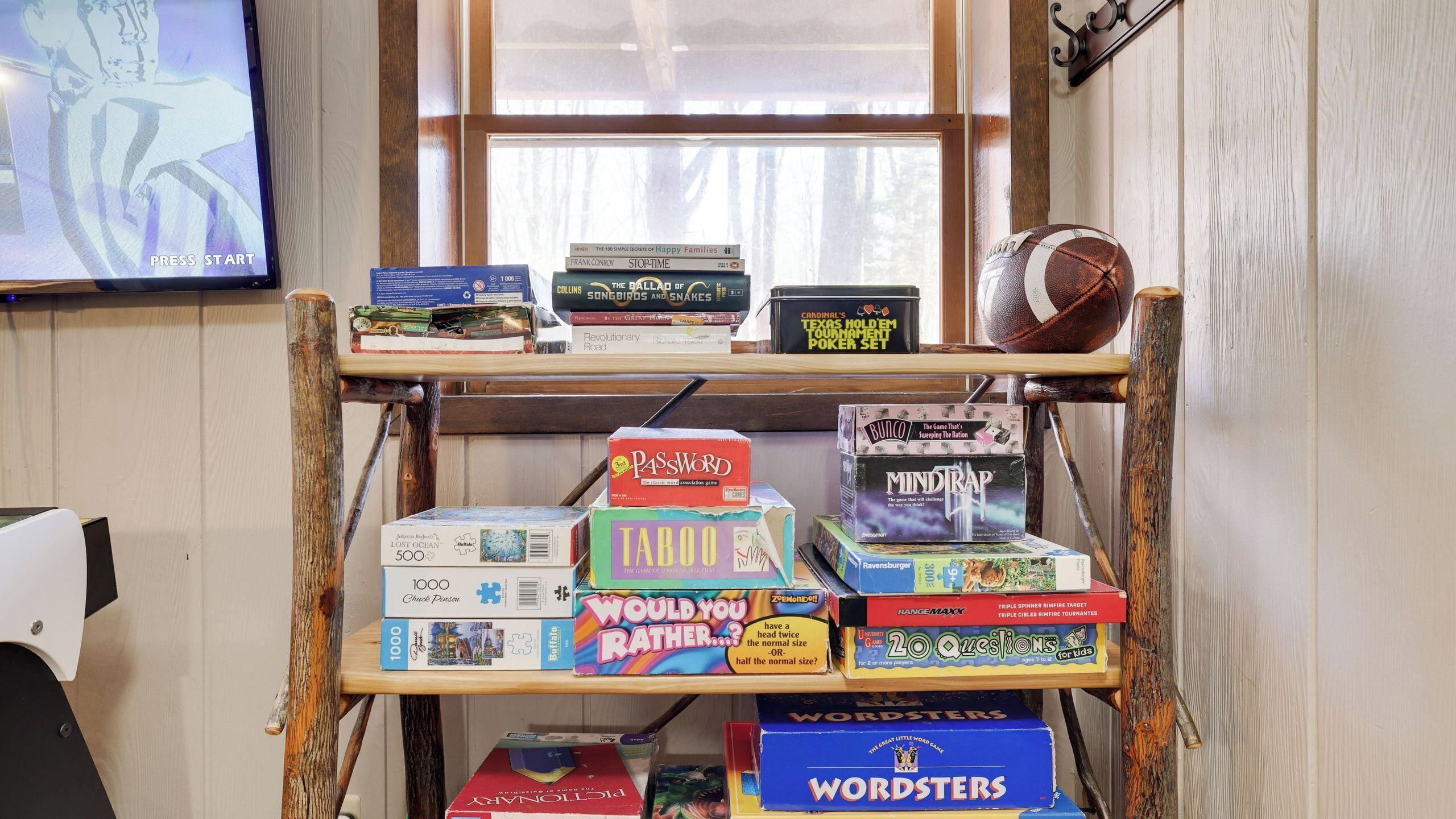 Un estante de madera con varios juegos de mesa y un televisor al fondo.