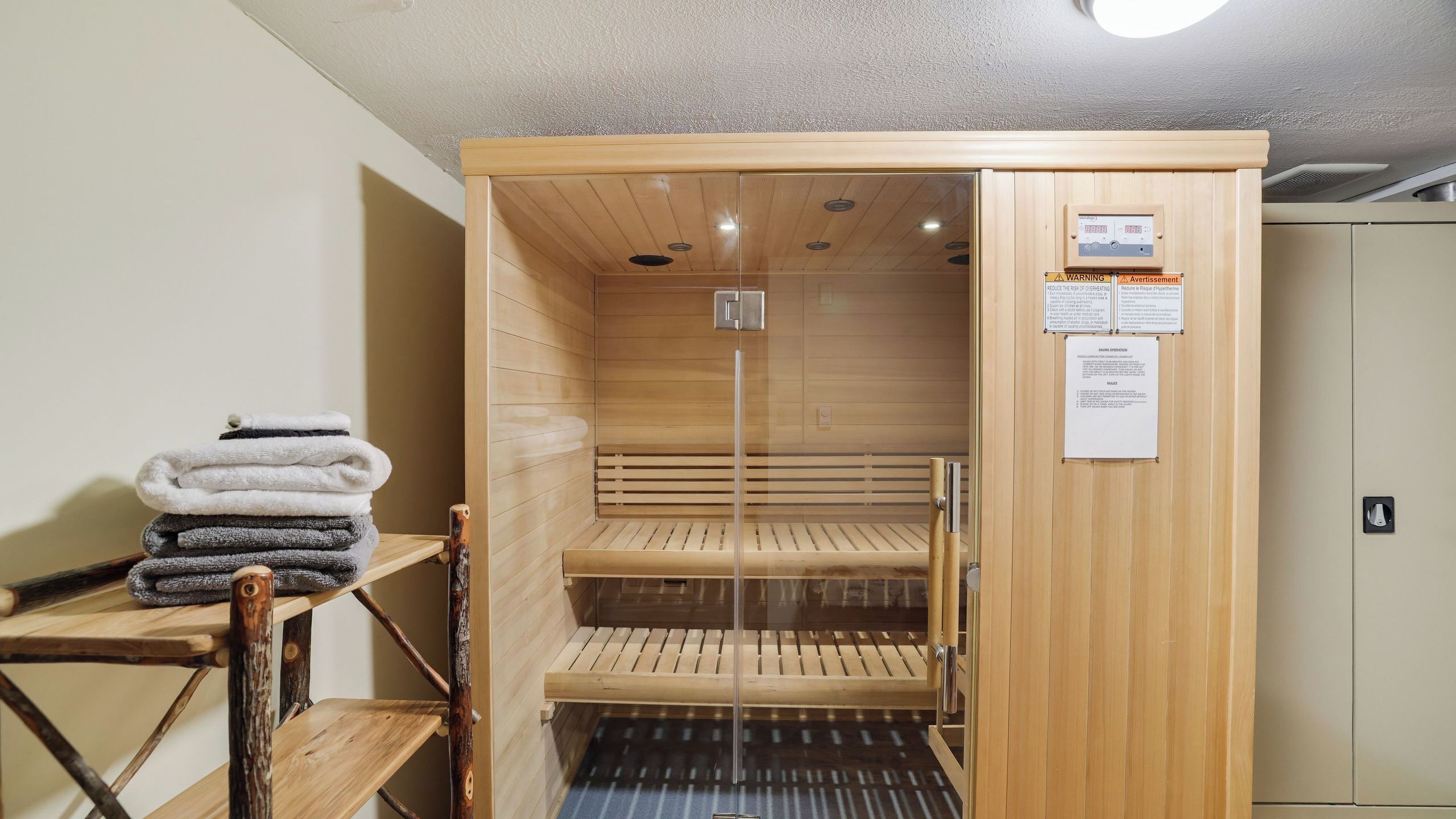 A sauna with wooden benches, a towel stack, and a control panel.