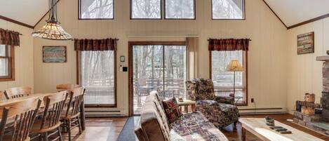 A spacious living room with a high ceiling, wooden furniture, and large windows.
